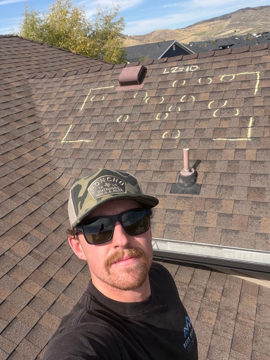 Spencer Beesley on a roof beside documented hail damage